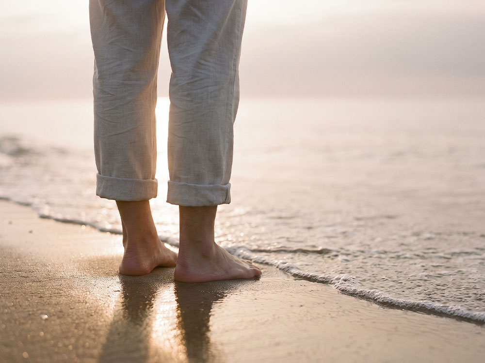 Nackte Füsse stehen ruhig im Sand am Wasser